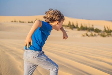 Çölde elinde akıllı bir telefonla dans eden sevimli, komik çocuk.