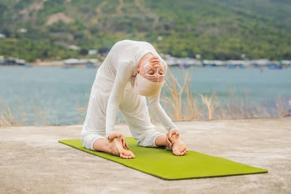 Kundalini yoga woman in white clothes and turban practices yoga kundalini on the background of the sea, mountains and sunset. Fighting face painting of the Indians shows her inner world. Visual