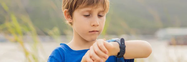 Niño utiliza los niños reloj inteligente al aire libre contra el fondo del jardín BANNER, FORMATO LARGO — Foto de Stock