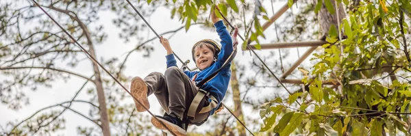 BANNER, LONG FORMAT Szczęśliwe dziecko w kasku, zdrowy młodzieniec szkolny cieszący się aktywnością w parku przygód wspinaczkowych w letni dzień — Zdjęcie stockowe