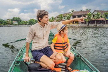Baba ve oğul turistler Tam Coc gölünde, Ninh Binh, Vietnam. UNESCO Dünya Mirası Alanı 'dır ve tekne mağarası turlarıyla ünlüdür. Vietnam topraklarındaki Halong Körfezi. Vietnam sınırları yeniden açıyor