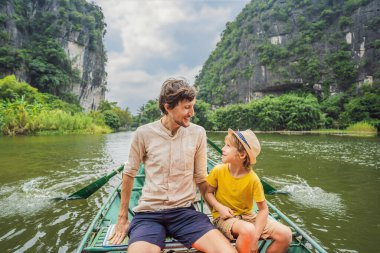 Baba ve oğul turistler Tam Coc gölünde, Ninh Binh, Vietnam. UNESCO Dünya Mirası Alanı 'dır ve tekne mağarası turlarıyla ünlüdür. Vietnam topraklarındaki Halong Körfezi. Vietnam sınırları yeniden açıyor