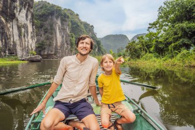 Baba ve oğul turistler Tam Coc gölünde, Ninh Binh, Vietnam. UNESCO Dünya Mirası Alanı 'dır ve tekne mağarası turlarıyla ünlüdür. Vietnam topraklarındaki Halong Körfezi. Vietnam sınırları yeniden açıyor