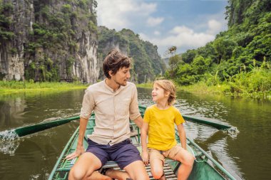 Baba ve oğul turistler Tam Coc gölünde, Ninh Binh, Vietnam. UNESCO Dünya Mirası Alanı 'dır ve tekne mağarası turlarıyla ünlüdür. Vietnam topraklarındaki Halong Körfezi. Vietnam sınırları yeniden açıyor