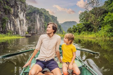 Baba ve oğul turistler Tam Coc gölünde, Ninh Binh, Vietnam. UNESCO Dünya Mirası Alanı 'dır ve tekne mağarası turlarıyla ünlüdür. Vietnam topraklarındaki Halong Körfezi. Vietnam sınırları yeniden açıyor
