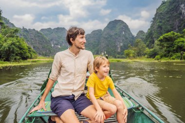 Baba ve oğul turistler Tam Coc gölünde, Ninh Binh, Vietnam. UNESCO Dünya Mirası Alanı 'dır ve tekne mağarası turlarıyla ünlüdür. Vietnam topraklarındaki Halong Körfezi. Vietnam sınırları yeniden açıyor