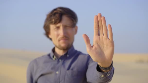 一个站在沙漠中的男人，在他面前拿着一把张开的手掌作为停止的标志。减少碳排放。停止气候变化 — 图库视频影像