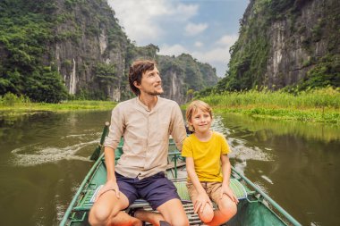Baba ve oğul turistler Tam Coc gölünde, Ninh Binh, Vietnam. UNESCO Dünya Mirası Alanı 'dır ve tekne mağarası turlarıyla ünlüdür. Vietnam topraklarındaki Halong Körfezi. Vietnam sınırları yeniden açıyor
