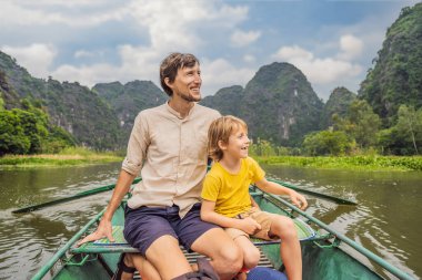 Baba ve oğul turistler Tam Coc gölünde, Ninh Binh, Vietnam. UNESCO Dünya Mirası Alanı 'dır ve tekne mağarası turlarıyla ünlüdür. Vietnam topraklarındaki Halong Körfezi. Vietnam sınırları yeniden açıyor