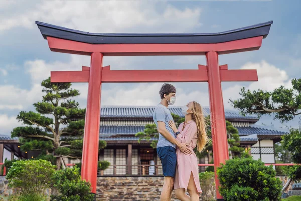 Feliz pareja de viajeros en máscara médica mirando el edificio tradicional japonés. Turistas viajan a Japón después de la epidemia de coronavirus —  Fotos de Stock