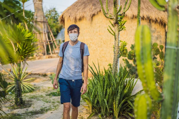 Beautiful stylish young man in desert among the cacti, wearing a medical mask during COVID-19 coronavirus, traveling in Africa on safari, exploring nature, sunny summer, traveler on vacation — Stock Photo, Image