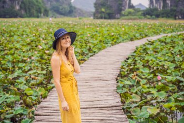 Lotus Gölü 'nün yanındaki yolda sarı elbiseli genç bir kadın. Mua Mağarası, Ninh Binh, Vietnam. Vietnam, Coronovirus COVID 19 konseptinden sonra yeniden açıldı.