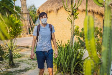 Kaktüslerin arasında çölde güzel bir genç adam, COVID-19 Coronavirus sırasında tıbbi maske takıyor, Afrika 'da safariye çıkıyor, doğayı keşfediyor, güneşli bir yaz, tatilde geziyor.