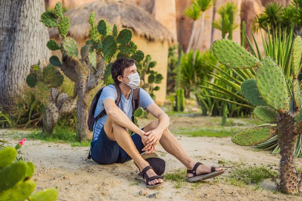 Schöner, stylischer junger Mann in Wüste inmitten der Kakteen, trägt während des COVID-19 Coronavirus eine medizinische Maske, reist auf Safari durch Afrika, erkundet die Natur, sonniger Sommer, Urlauber — Stockfoto