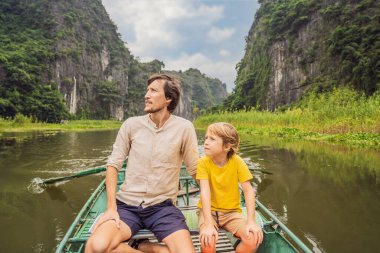 Baba ve oğul turistler Tam Coc gölünde, Ninh Binh, Vietnam. UNESCO Dünya Mirası Alanı 'dır ve tekne mağarası turlarıyla ünlüdür. Vietnam topraklarındaki Halong Körfezi. Vietnam sınırları yeniden açıyor
