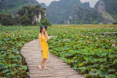 Lotus Gölü 'nün yanındaki yolda sarı elbiseli genç bir kadın. Mua Mağarası, Ninh Binh, Vietnam. Vietnam, Coronovirus COVID 19 konseptinden sonra yeniden açıldı.