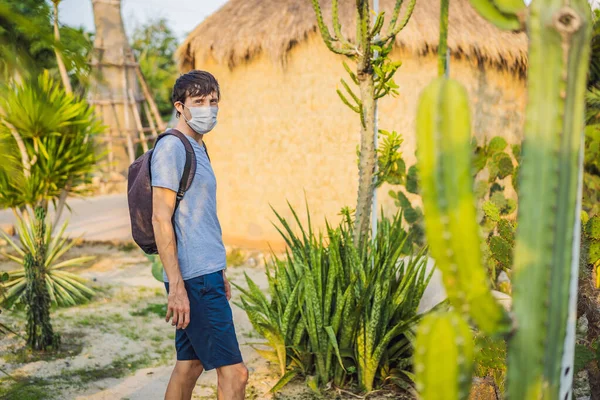 Beautiful stylish young man in desert among the cacti, wearing a medical mask during COVID-19 coronavirus, traveling in Africa on safari, exploring nature, sunny summer, traveler on vacation — Stock Photo, Image