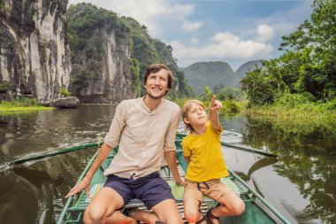 Baba ve oğul turistler Tam Coc gölünde, Ninh Binh, Vietnam. UNESCO Dünya Mirası Alanı 'dır ve tekne mağarası turlarıyla ünlüdür. Vietnam topraklarındaki Halong Körfezi. Vietnam sınırları yeniden açıyor