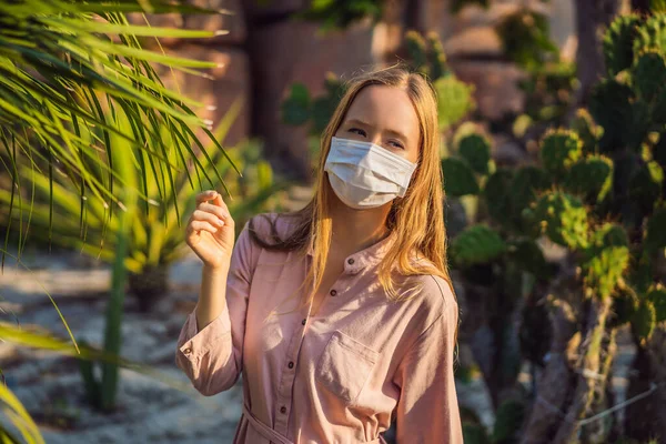 Bela jovem elegante em vestido rosa no deserto entre os cactos, vestindo uma máscara médica durante COVID-19 coronavírus, viajando na África em safári, explorando a natureza, verão ensolarado, viajante em — Fotografia de Stock