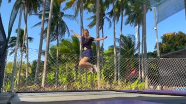 Yavaş çekim yap. Genç bir kadın tropik bölgelerdeki trambolin parkında eğleniyor. Telefonla vurulmuş.