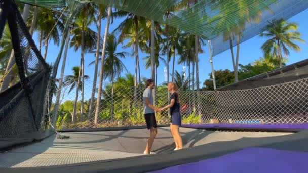 Zpomalený výstřel. Mladý muž a žena se baví v trampolínovém parku v tropech. Zastřelen na telefonu — Stock video