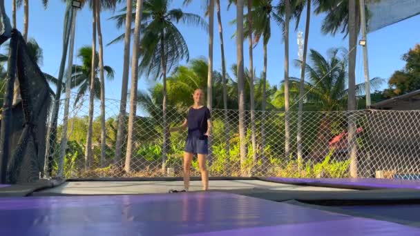 Yavaş çekim yap. Genç bir kadın tropik bölgelerdeki trambolin parkında eğleniyor. Telefonla vurulmuş. — Stok video