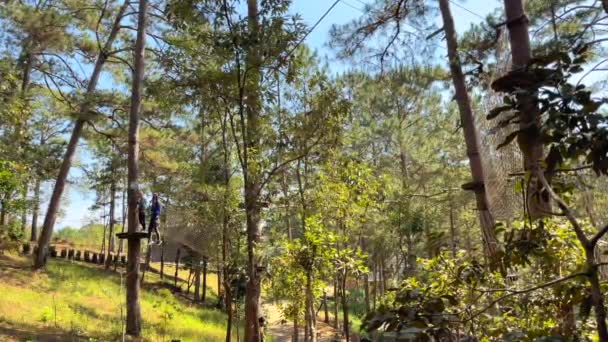 Slowmotion tiro de um menino em um capacete amarelo que está se divertindo em um parque de aventura escalada corda — Vídeo de Stock