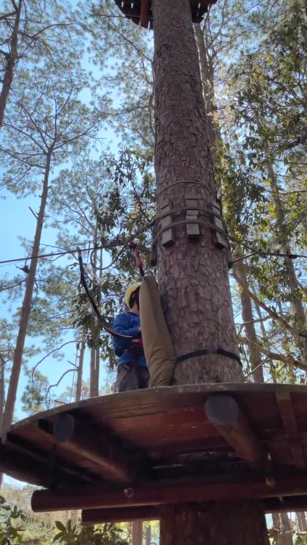 Vertical video. Slowmotion shot of a boy in a yellow helmet that is having fun in a rope climbing adventure park — Stock Video