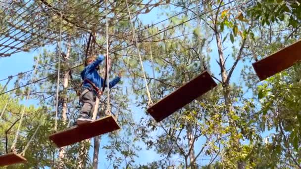 Slowmotion tiro de um menino em um capacete amarelo que está se divertindo em um parque de aventura escalada corda — Vídeo de Stock