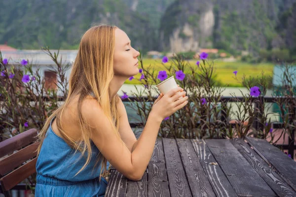 Kobieta pije rano kawę na tle wzgórz w Ninh Binh, Tam Coc. Wznowienie turystyki w Wietnamie po kwarantannie Coronovirus COVID 19 — Zdjęcie stockowe
