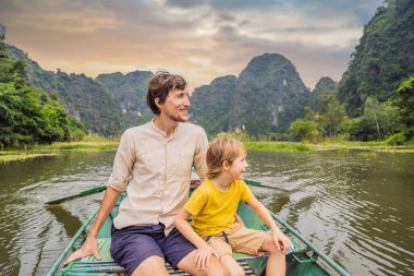 Baba ve oğul turistler Tam Coc gölünde, Ninh Binh, Vietnam. UNESCO Dünya Mirası Alanı 'dır ve tekne mağarası turlarıyla ünlüdür. Vietnam topraklarındaki Halong Körfezi. Vietnam sınırları yeniden açıyor