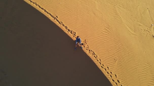 Tiro aéreo de um homem sentado numa duna de areia num deserto — Vídeo de Stock
