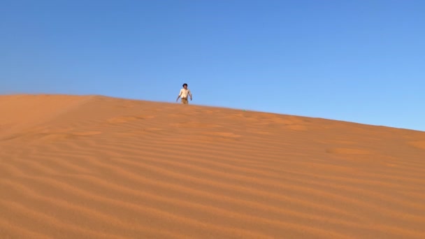 Fotografía en cámara lenta de un hombre divertido que se divierte corriendo por la duna en un desierto — Vídeos de Stock