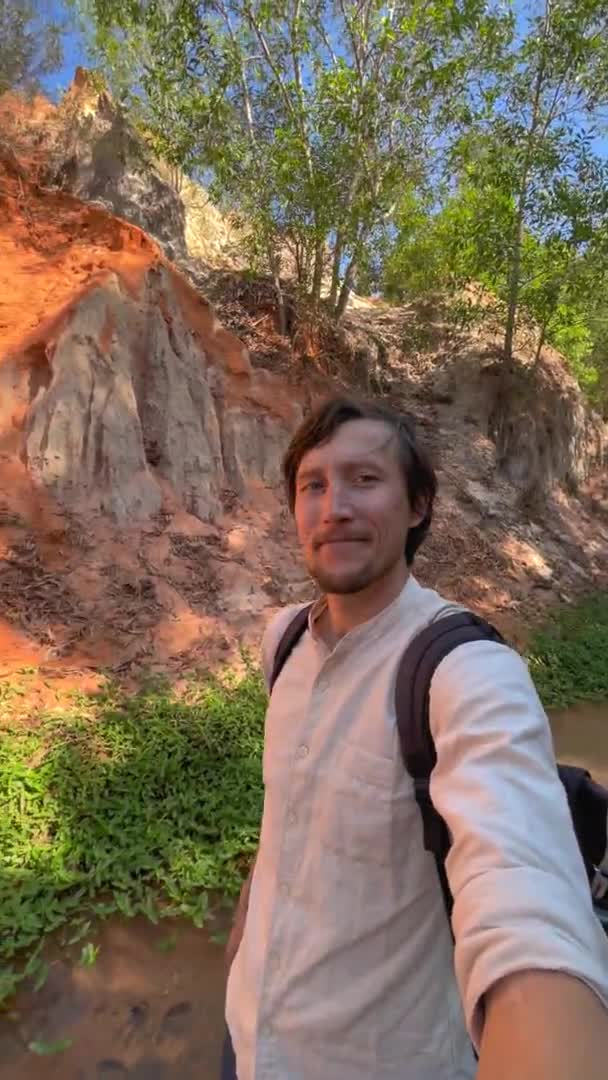 Vidéo verticale. Tir au ralenti. Un touriste homme visite le canyon rouge ou ruisseau de la Fée à la frontière du désert dans le village de Mui Ne dans le sud du Vietnam. Tourné sur un téléphone. — Video