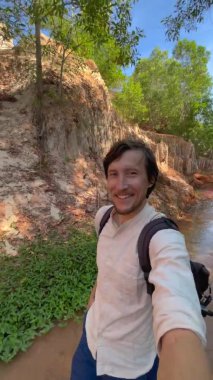 Dikey video. Yavaş çekim yap. Bir erkek turist, Vietnam 'ın güneyindeki Mui Ne köyündeki çöl sınırındaki kırmızı kanyon ya da peri deresini ziyaret ediyor. Telefonla vurulmuş..