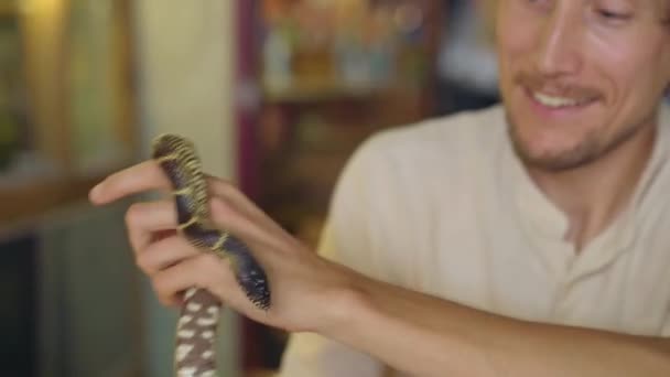 En man besöker ett café med exotiska djur. Café där du kan komma i kontakt med djur. Han rör vid en orm.. — Stockvideo