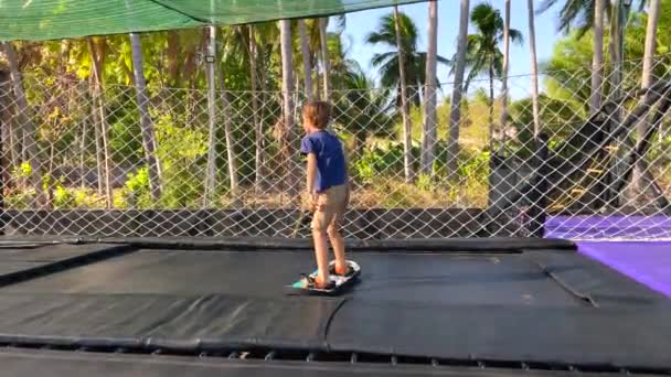 Zpomalený výstřel. Malý chlapec se baví v trampolínovém parku v tropech. Zastřelen na telefonu — Stock video