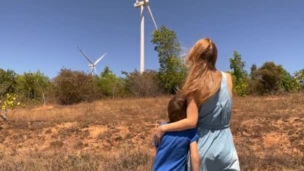 Tiro em câmara lenta. Jovem e seu filho visitam um parque de turbinas eólicas em um ambiente semideserto. Conceito de energia eólica — Vídeo de Stock