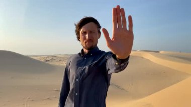 Çölde, elinde dur işareti olarak bir avuç içi açık duran bir adamın yavaş çekim sahnesi. Karbon salınımını azaltın. İklim değişikliğini durdur