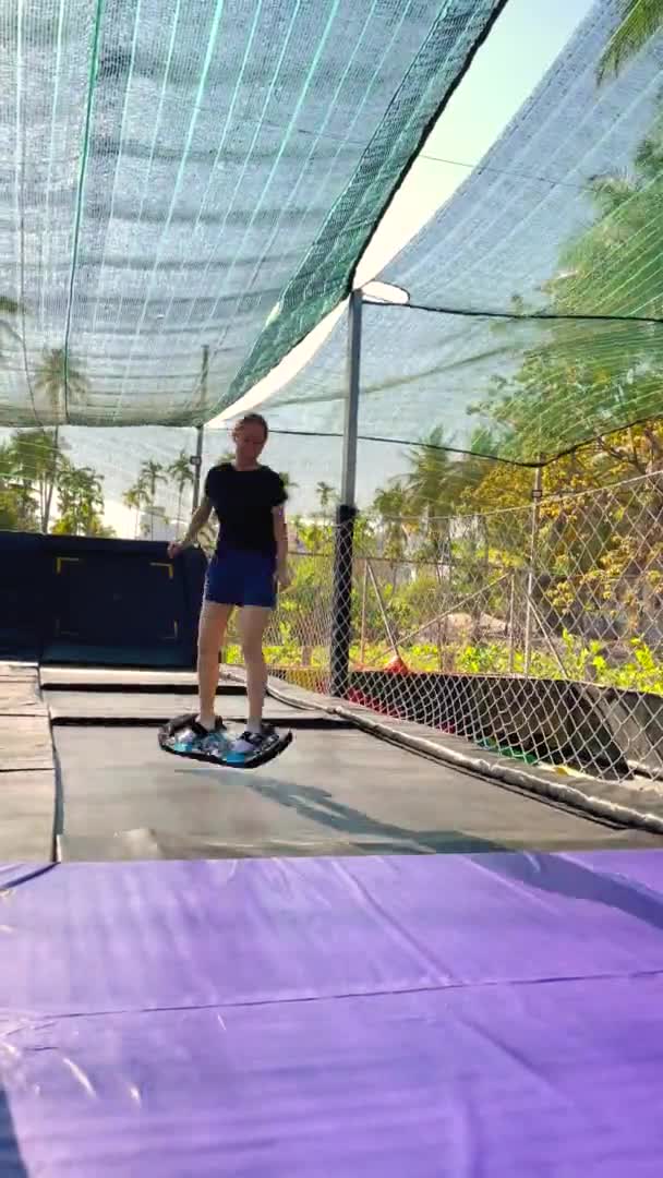 Vertikal video. Slowmotion-skott. En ung kvinna har kul i en trampolinpark i tropikerna. Skjuten på en telefon — Stockvideo