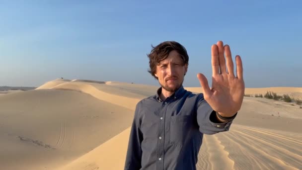 Fotografía en cámara lenta de un hombre de pie en un desierto que sostiene una palma abierta frente a él como señal de stop. Reducir las emisiones de carbono. Detener el cambio climático — Vídeos de Stock