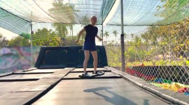 Yavaş çekim yap. Genç bir kadın tropik bölgelerdeki trambolin parkında eğleniyor. Telefonla vurulmuş.