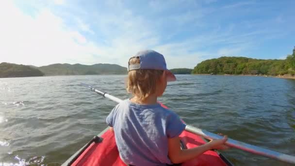 Plan au ralenti d'un mignon petit garçon pagayant dans un kayak gonflable — Video