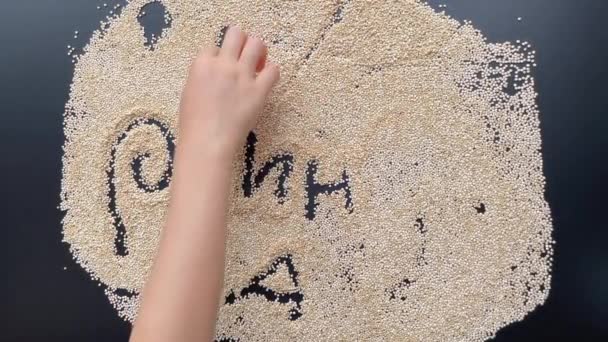 A little boy is writing letters on a blackboard covered with quinoa seeds — Stock Video