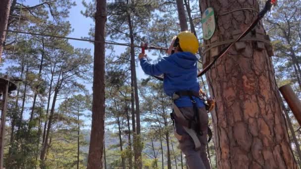 Zpomalení záběr chlapce ve žluté helmě, která se baví v laně horolezectví dobrodružství park. Zastřelen na telefonu — Stock video