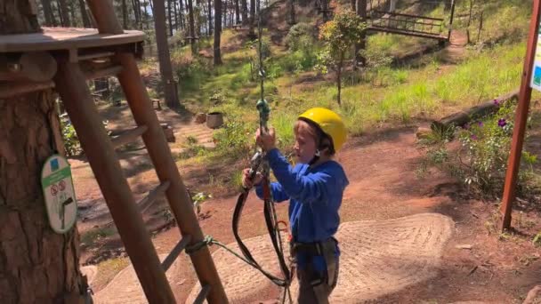 Zpomalení záběr chlapce ve žluté helmě, která se baví v laně horolezectví dobrodružství park. Zastřelen na telefonu — Stock video