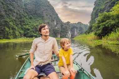 Baba ve oğul turistler Tam Coc gölünde, Ninh Binh, Vietnam. UNESCO Dünya Mirası Alanı 'dır ve tekne mağarası turlarıyla ünlüdür. Vietnam topraklarındaki Halong Körfezi. Vietnam sınırları yeniden açıyor