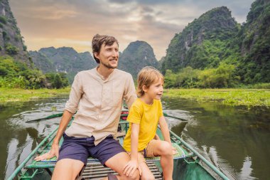 Baba ve oğul turistler Tam Coc gölünde, Ninh Binh, Vietnam. UNESCO Dünya Mirası Alanı 'dır ve tekne mağarası turlarıyla ünlüdür. Vietnam topraklarındaki Halong Körfezi. Vietnam sınırları yeniden açıyor