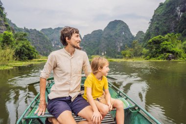 Baba ve oğul turistler Tam Coc gölünde, Ninh Binh, Vietnam. UNESCO Dünya Mirası Alanı 'dır ve tekne mağarası turlarıyla ünlüdür. Vietnam topraklarındaki Halong Körfezi. Vietnam sınırları yeniden açıyor
