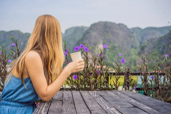 Kobieta pije rano kawę na tle wzgórz w Ninh Binh, Tam Coc. Wznowienie turystyki w Wietnamie po kwarantannie Coronovirus COVID 19 — Zdjęcie stockowe